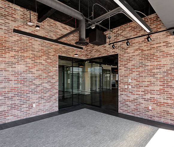 Office corner with large windows and exposed brick wall.