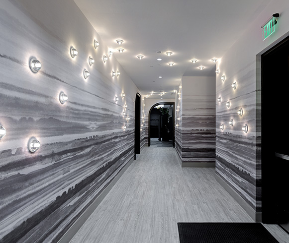 A hallway with grey accents and grey floors with small light features on the walls and ceiling.