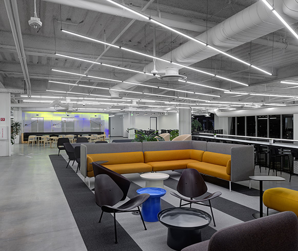Open seating with an orange and grey couch with black chairs for employees to use.