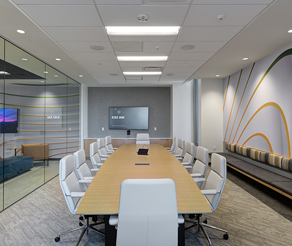 A large conference room with one long wood table and white chairs.