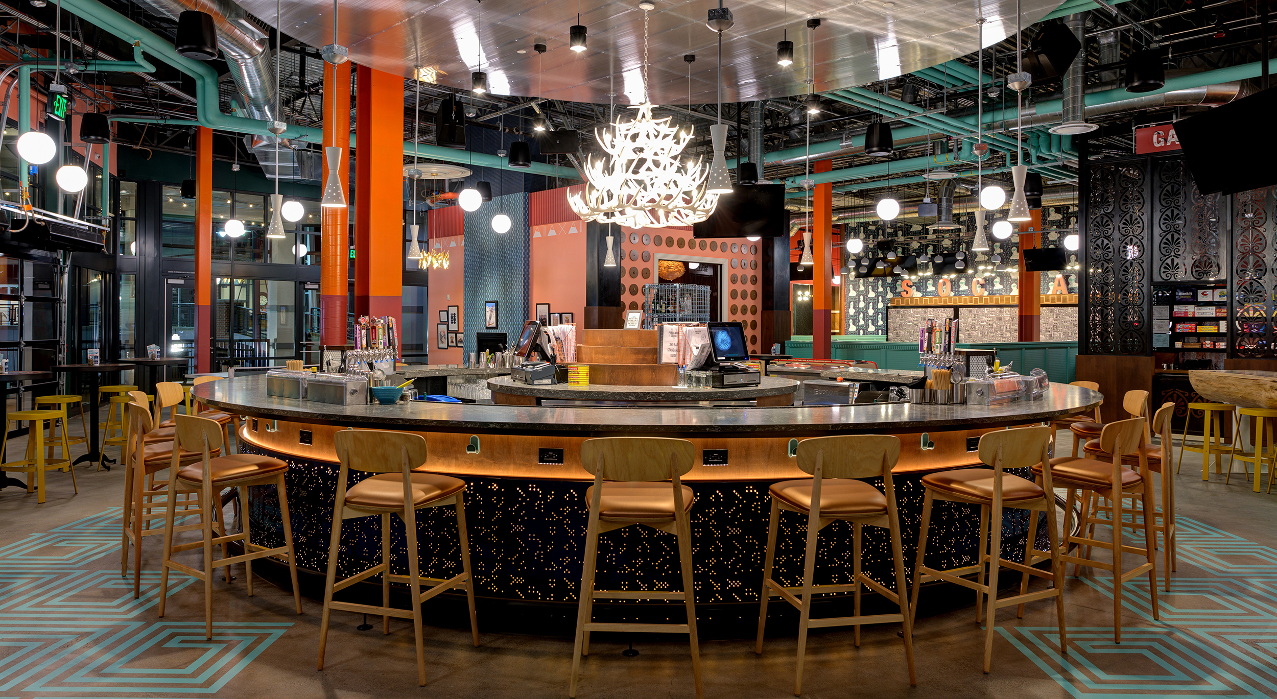 A round bar in the center of a room with a chandelier and colorful painted features.
