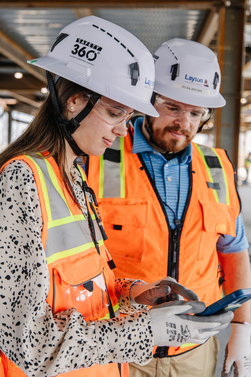 Two Layton employees in PPE on site looking at plans on a cell phone.