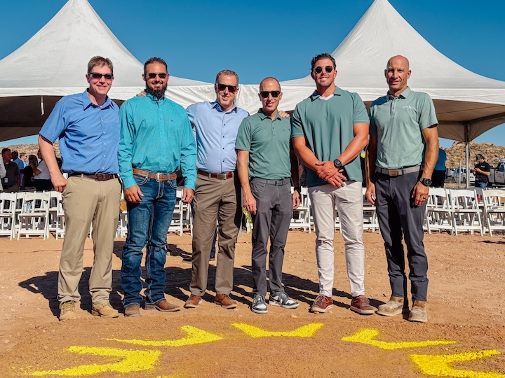 Six members of the Layton Construction team stand together smiling at the groundbreaking site for the St. George Regional Airport air traffic control tower, with white event tents and chairs in the background.
